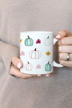 a woman holding a coffee mug with pumpkins on it