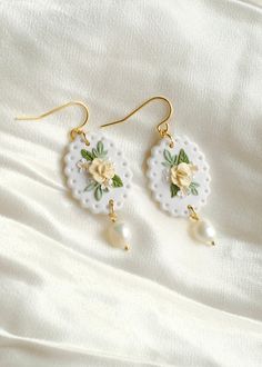 the earrings are decorated with flowers and pearls on white fabric, along with gold - plated earwires