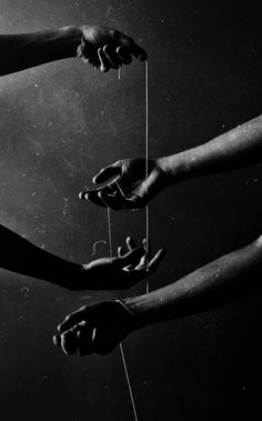 four hands reaching for something with string attached to it in black and white photo, against dark background