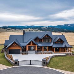 a large home in the middle of an open field with mountains in the back ground