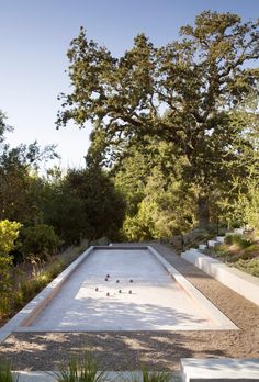 an empty pool in the middle of a garden with trees and bushes around it, surrounded by gravel