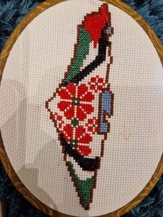 a cross stitch pattern on a wooden hoop hanging from a blue rug with a red, white and green christmas ornament