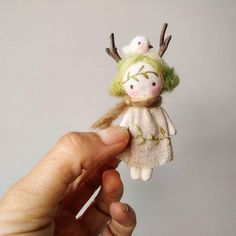 a hand holding a small doll with green hair and antlers on it's head