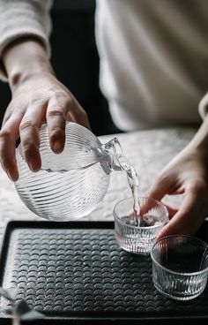 a person pouring water from a pitcher into a glass on top of a black tray