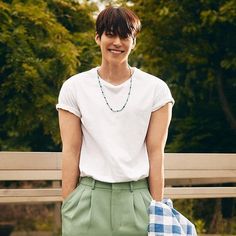 a young man standing in front of a park bench wearing green shorts and a white t - shirt