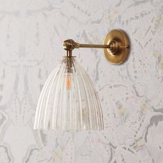 a wall light with a clear glass shade on it's arm and an antique brass finish