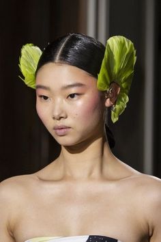 a woman with black hair wearing a green flower in her hair on the catwalk