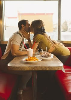 a man and woman sitting at a table sharing a kiss in front of a window