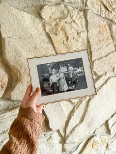 a person holding up an old photo in front of a stone wall