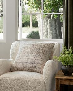 a white chair sitting in front of a window next to a wooden table with a potted plant on it