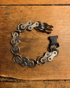 a close up of a metal bracelet on a wooden surface with a black clasp and two silver chains