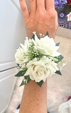 a woman's arm with white flowers and greenery attached to the wrist area