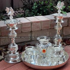 two silver candlesticks sitting on top of a metal tray next to a brick wall