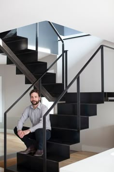 a man sitting on top of a black stair case next to a white wall and wooden floor