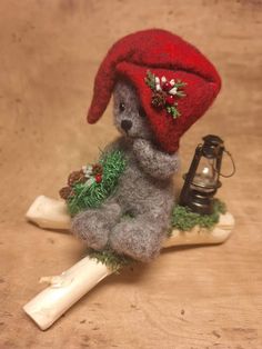 a small stuffed animal wearing a red hat sitting on a piece of wood with a lantern in the background