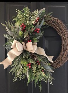 a christmas wreath with pine cones, berries and greenery hanging on the front door