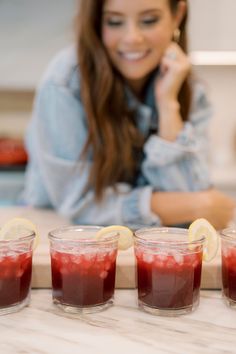 a woman sitting at a counter with four glasses filled with liquid