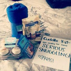 an assortment of food items on a bed with a sign that reads cuddle kit get ready for some serious snuggling