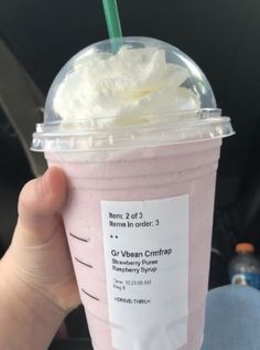 a person holding up a pink drink with whipped cream on top