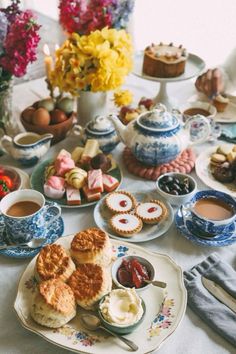 a table topped with plates and cups filled with desserts next to flowers on top of a white table cloth