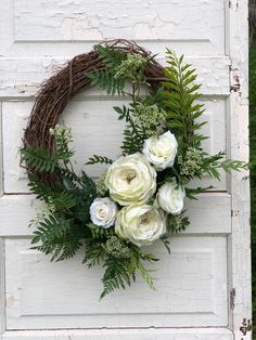 a wreath with white flowers and greenery hangs on the side of an old door