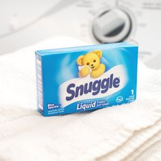 a box of snuggle liquid sitting on top of a pile of white towels