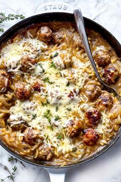 a skillet filled with meatballs and pasta on top of a marble countertop