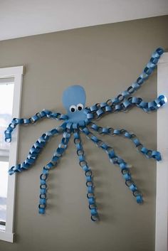 a blue octopus made out of plastic cups on the side of a wall with a window in the background