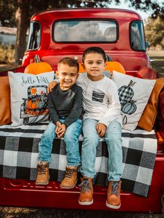 two young boys sitting on the back of a red pickup truck with pumpkins in the bed