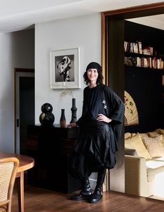 a woman standing in a living room next to a wooden table and bookshelf