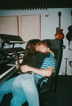 a man and woman kissing in front of an electronic keyboard with guitars on the wall behind them