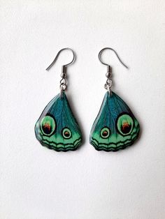 a pair of green and black butterfly earrings on a white surface with silver earwires