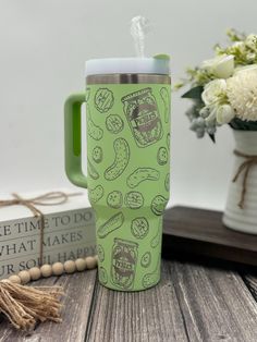 a green coffee mug sitting on top of a wooden table next to a vase with flowers