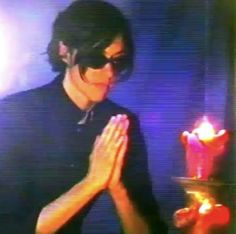 a man in black shirt and sunglasses holding a lit candle with both hands while standing next to him