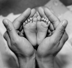 two hands are holding the feet of a baby's foot in black and white