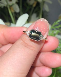 a woman's hand holding a ring with a green stone and diamond on it