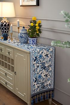 a blue and white table cloth sitting on top of a wooden cabinet next to a vase with yellow flowers