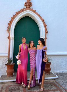 three beautiful women standing next to each other in front of a green door wearing dresses