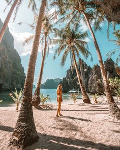 a woman standing on top of a sandy beach next to palm tree covered mountains and water