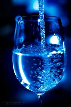 a wine glass filled with water on top of a blue tablecloth and black background