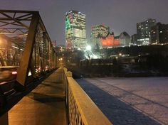 the city skyline is lit up at night as cars drive over a bridge in the snow