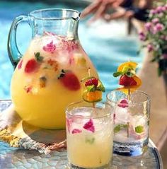 a pitcher and two glasses filled with fruit on top of a table next to a pool