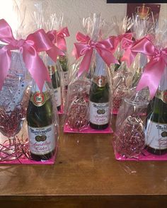 three bottles of champagne in plastic bags on a table with pink bows and ribbons around them