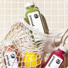 three bottles of juice sitting in a net bag next to each other on a tiled surface