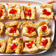 small pastries are arranged on a white platter with red sauce and green sprigs