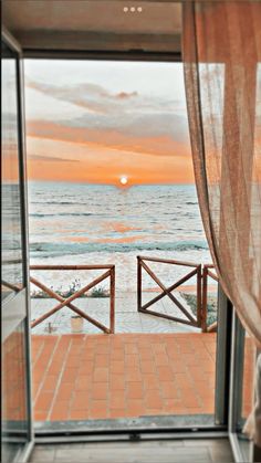 an open door leading out to the ocean at sunset or sunrise with curtains on either side