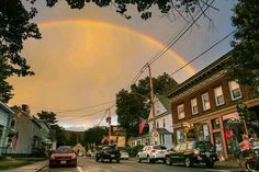 a rainbow is seen in the sky over a street with parked cars and people on bikes