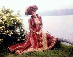 a woman in a red and gold dress is sitting on the grass near some flowers