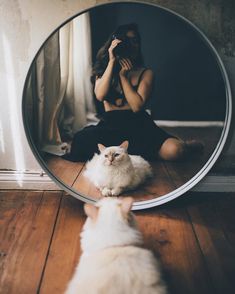 a white cat laying on the floor in front of a mirror with a woman looking at it