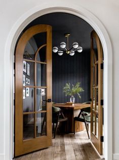 an open door leading to a dining room with wooden floors and black walls, in the middle of a hallway